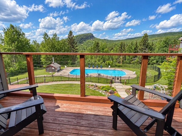 Una terraza de madera con dos sillas, una piscina y un patio cercado con una pequeña construcción.