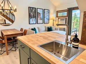 Een moderne keuken met een houten aanrecht, een roestvrijstalen spoelbak en een eethoek met een houten tafel en stoelen.