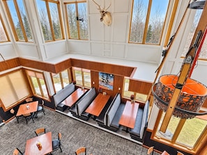 Un restaurant avec de hauts plafonds, de grandes fenêtres et différents types de sièges, notamment des banquettes et des tables.