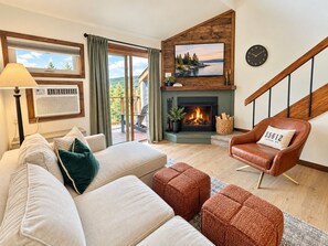 A living room with a fireplace, a sofa, a chair, and a view of the outdoors. - Beautiful Mountainview Top Floor Loft | Ski-in/out (Lutsen)