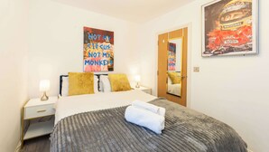 A hotel room with a bed, two bedside tables, a nightstand, a mirror, and two wall art pieces.