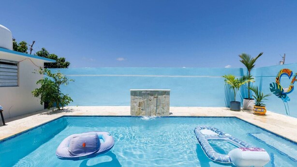 Ein Swimmingpool mit zwei aufblasbaren Schwimmringen, einer Steinstruktur und Blick aufs Meer.