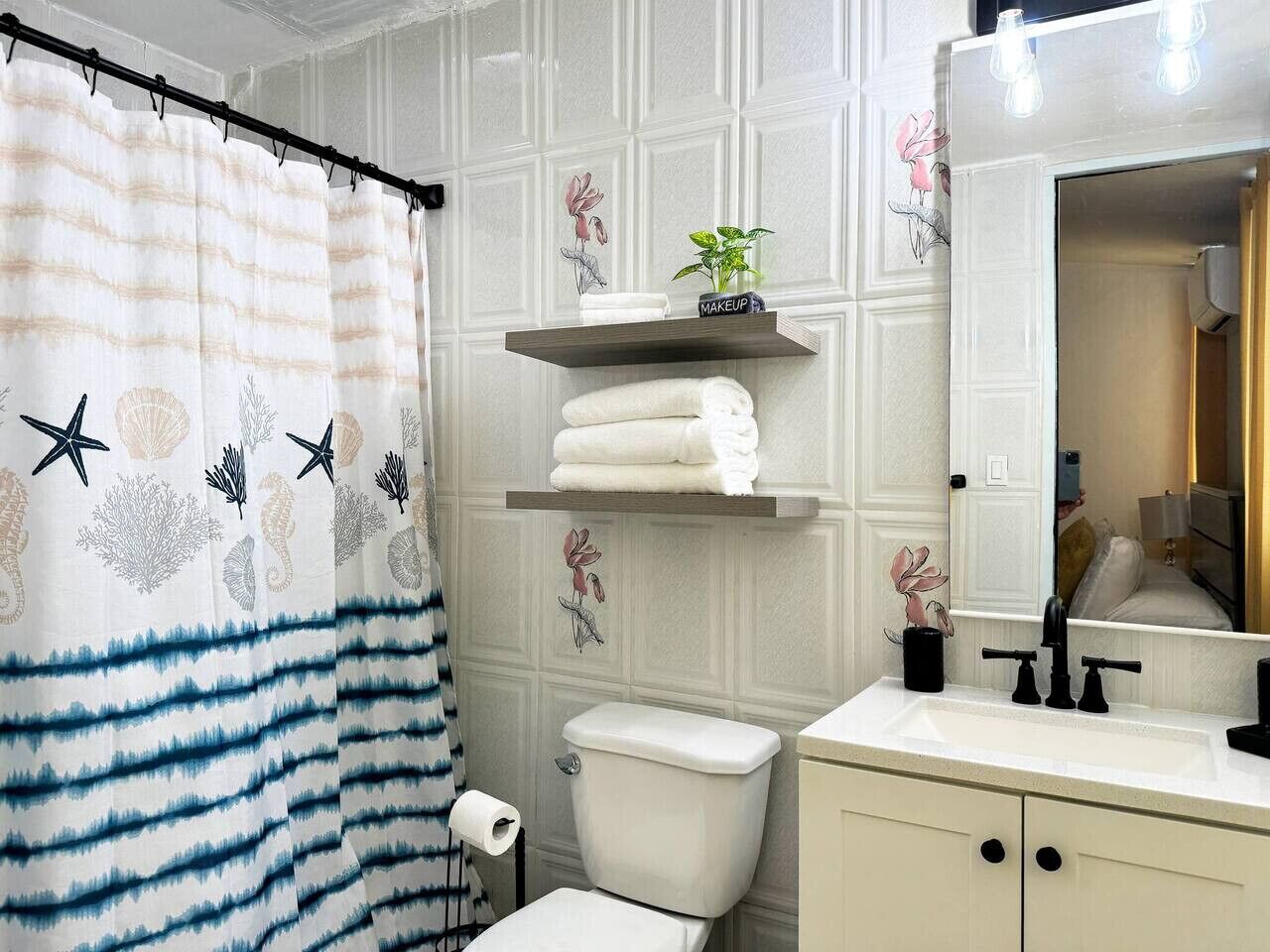 Un baño con cortina de ducha a rayas, inodoro, lavamanos con espejo y estantes decorativos con toallas y una planta.