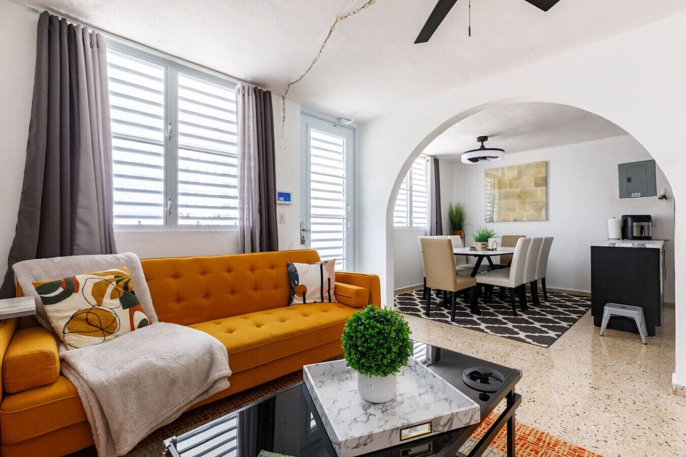 A modern living room with a sofa, a coffee table, and a dining area with chairs and a table.