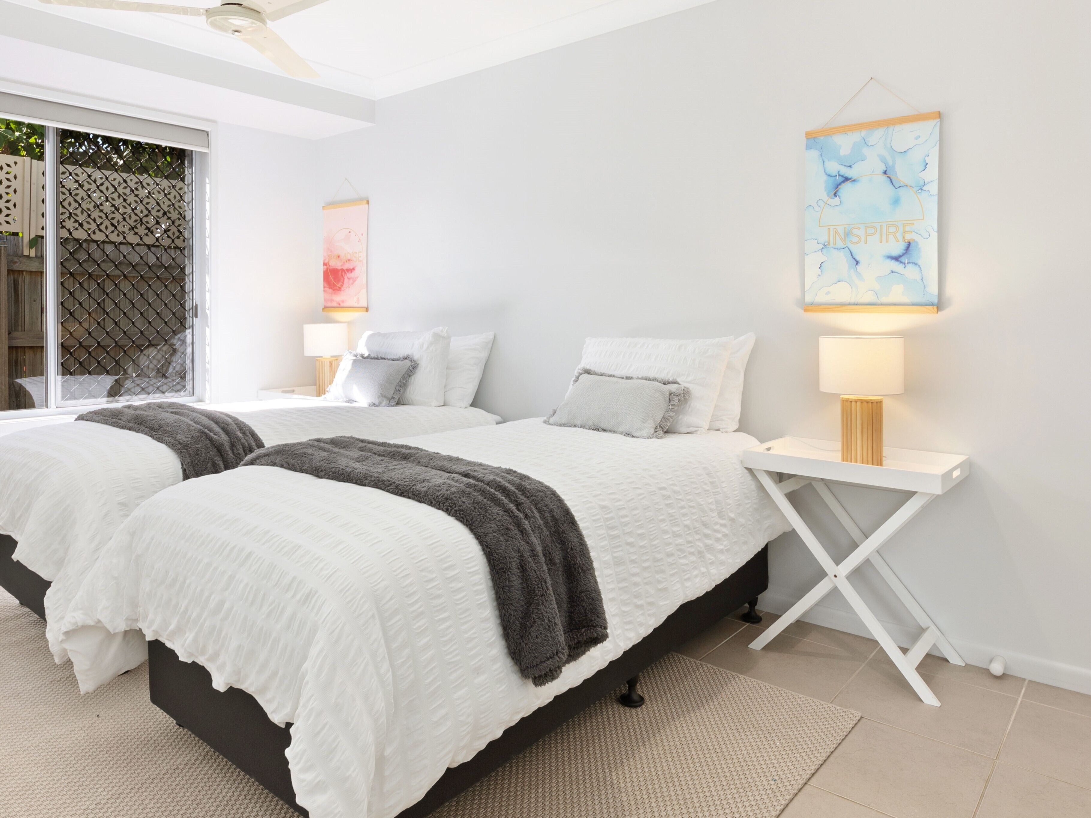 A modern bedroom with two beds, white bedding, and a small bedside table with a lamp.
