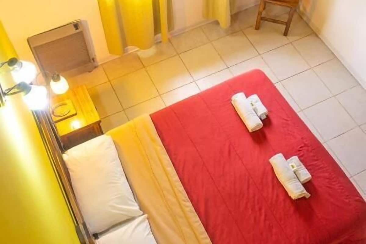 Una habitación de hotel con cama, una silla, una mesa con lámpara y una ventana con cortinas.