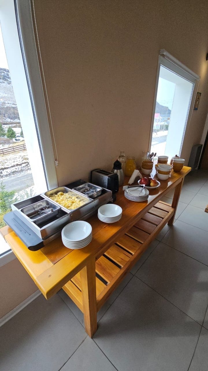 Disposición de un bufé con varios recipientes y tazones de comida sobre una mesa de madera, cerca de una ventana con vista al exterior.