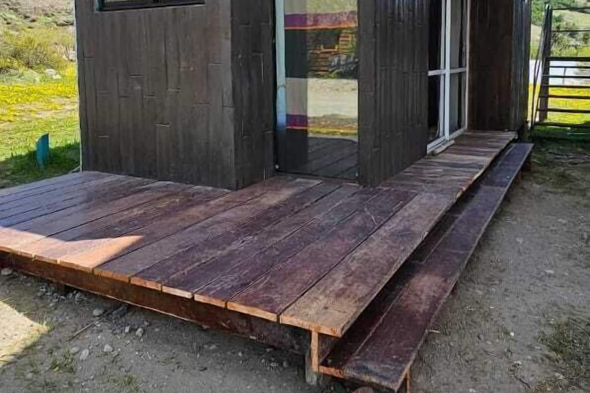Una cabaña moderna de madera con una amplia terraza, una entrada con puerta de vidrio y vistas del paisaje circundante.