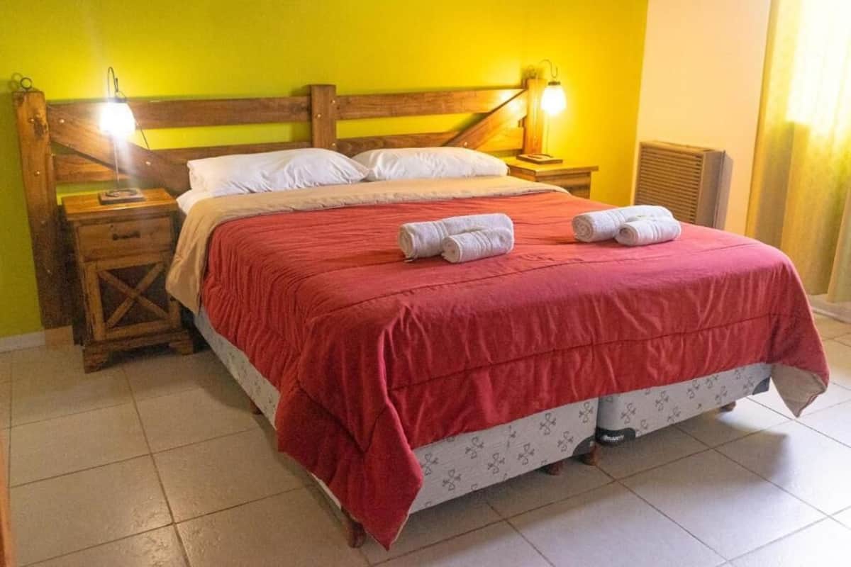 Una cama con colcha roja, dos lámparas de noche y un cabecero de madera.