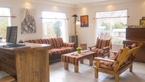Un salon spacieux comprenant un canapé, des fauteuils, une table basse en bois et un bureau avec un ordinateur portable.