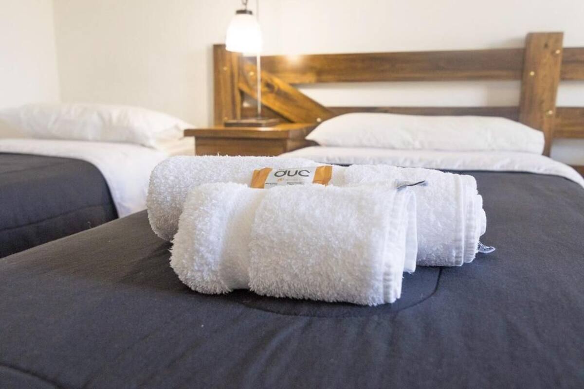 Una cama bien hecha con una toalla blanca y una etiqueta con la inscripción 'OUC' sobre una colcha oscura.