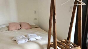 Une chambre avec un cadre de lit en bois, un portant à vêtements suspendu et un lit recouvert d’une couverture beige.
