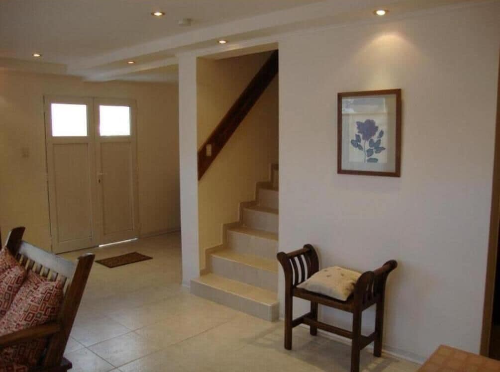 Un amplio espacio habitable con una escalera, una obra de arte enmarcada en la pared y una silla de madera.
