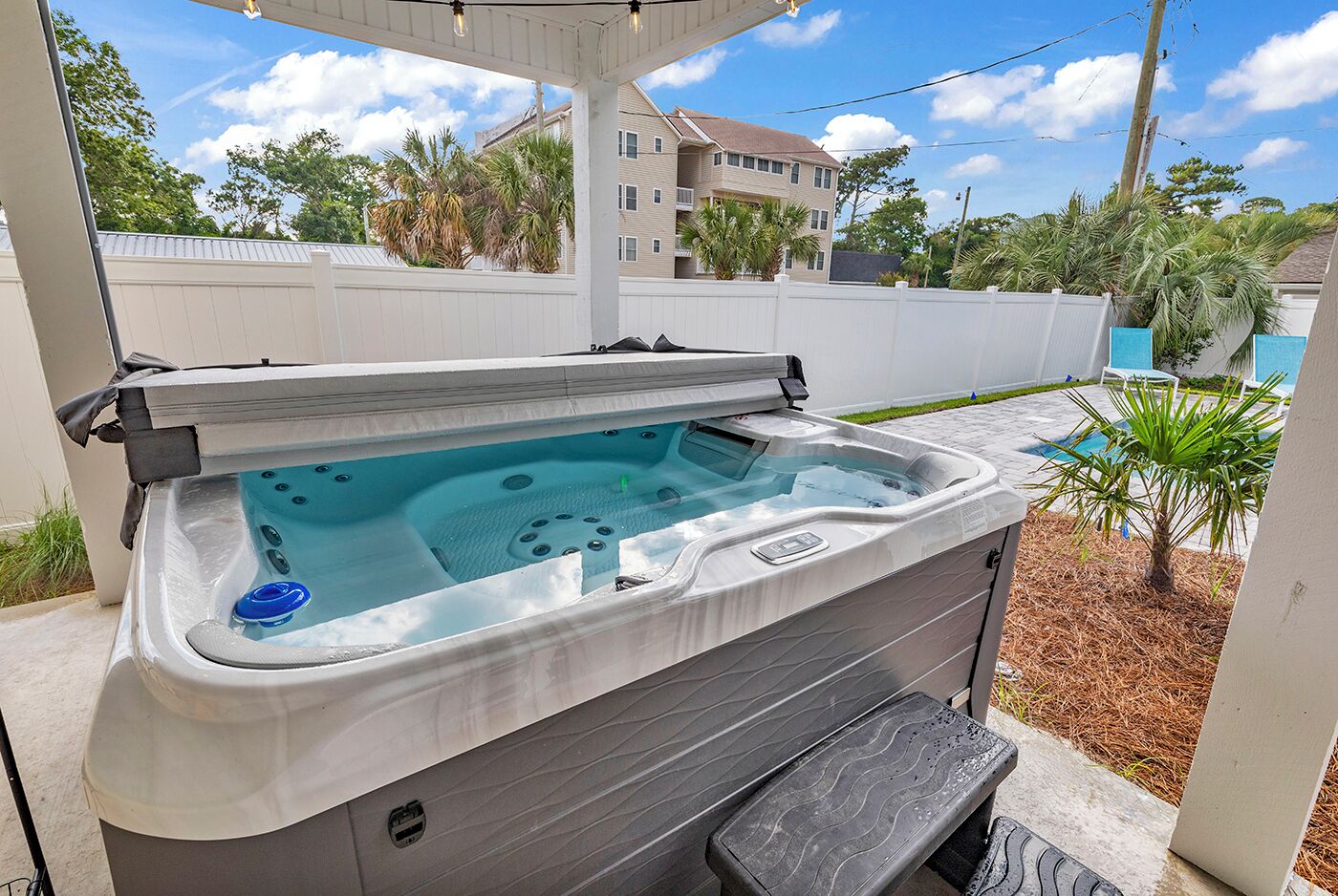 A hot tub with a cover, a step, and a pool in the background.