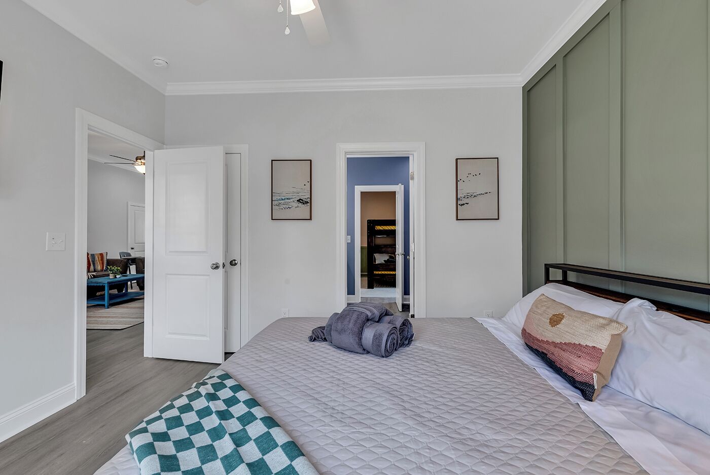 Une chambre à coucher avec un lit, un banc à carreaux, une porte donnant sur une salle de bain et un couloir avec une porte bleue.