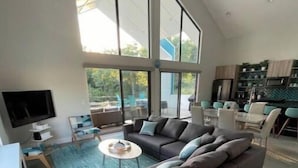 Een ruime woonkamer met een grote hoekbank, een flatscreen televisie aan de muur en een eethoek met een tafel en stoelen.