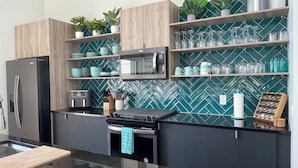 Een moderne keuken met een zwarte koelkast, een magnetron en een fornuis. Er staan planken met glazen en planten.