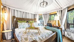 Ein gemütliches Zelt-Schlafzimmer mit einem hölzernen Bett, einem Nachttisch mit Lampe und Blick ins Freie.
