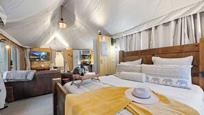 Alojamiento tipo tienda de campaña con cama, sofá, zona de comedor y televisión.