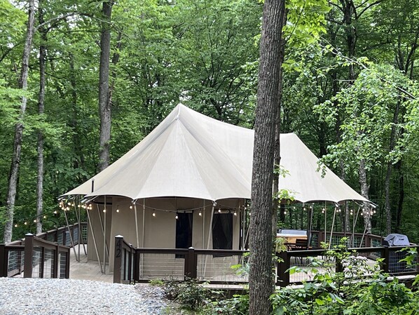 A tented structure with a covered entrance, a wooden deck, and a grill area.