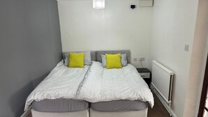 A small, neatly arranged bedroom with two single beds, a radiator, and a power outlet on the wall. - 1 Bedroom - Sleeps 3 - Free Parking (Luton)