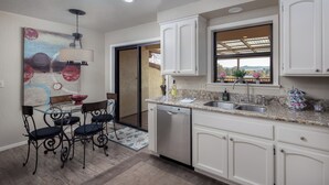 A modern kitchen with white cabinets, a granite countertop, a dishwasher, and a window with a view.