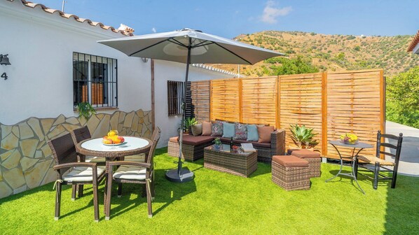 Une terrasse avec une table ronde, des chaises en osier, un canapé et une clôture en bois.