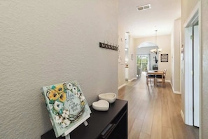 A hallway with a painting, a coat rack, and a dining area in the background.