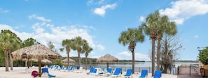 A beach with lounge chairs, thatched umbrellas, and palm trees.