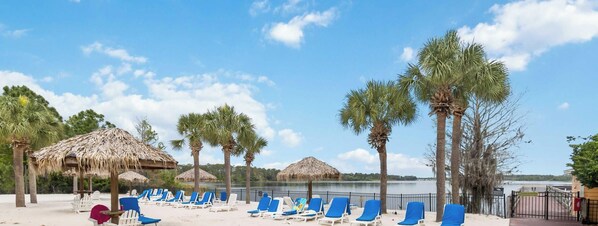 A beach with lounge chairs, palm trees, and thatched umbrellas. - Beautiful condo in Bahama Bay (Davenport)