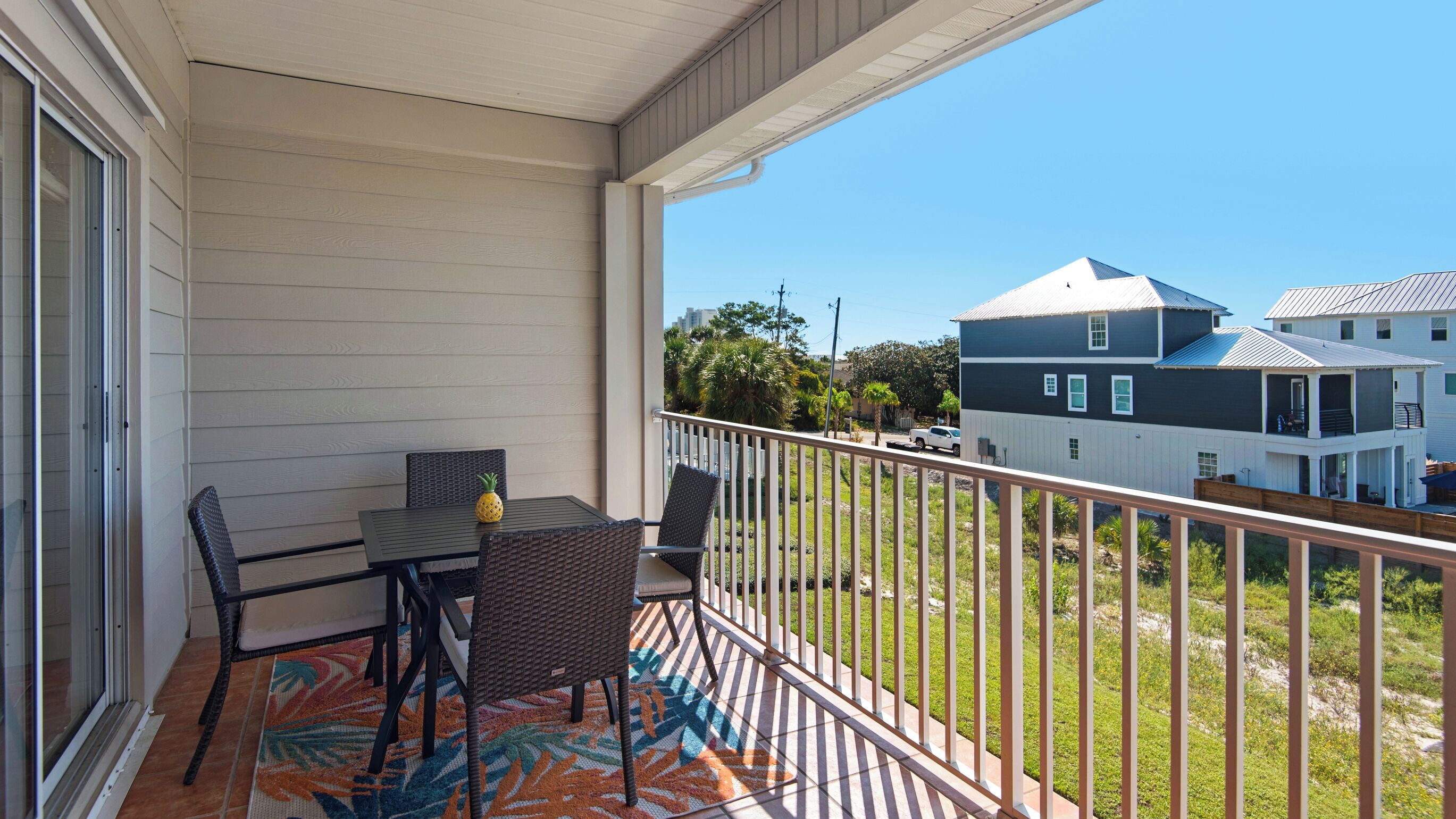 A balcony with a table and chairs, a patterned rug, and a view of neighboring houses.