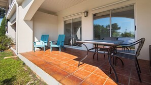 Une terrasse extérieure avec une table et des chaises, une porte-fenêtre coulissante et une vue sur la verdure.
