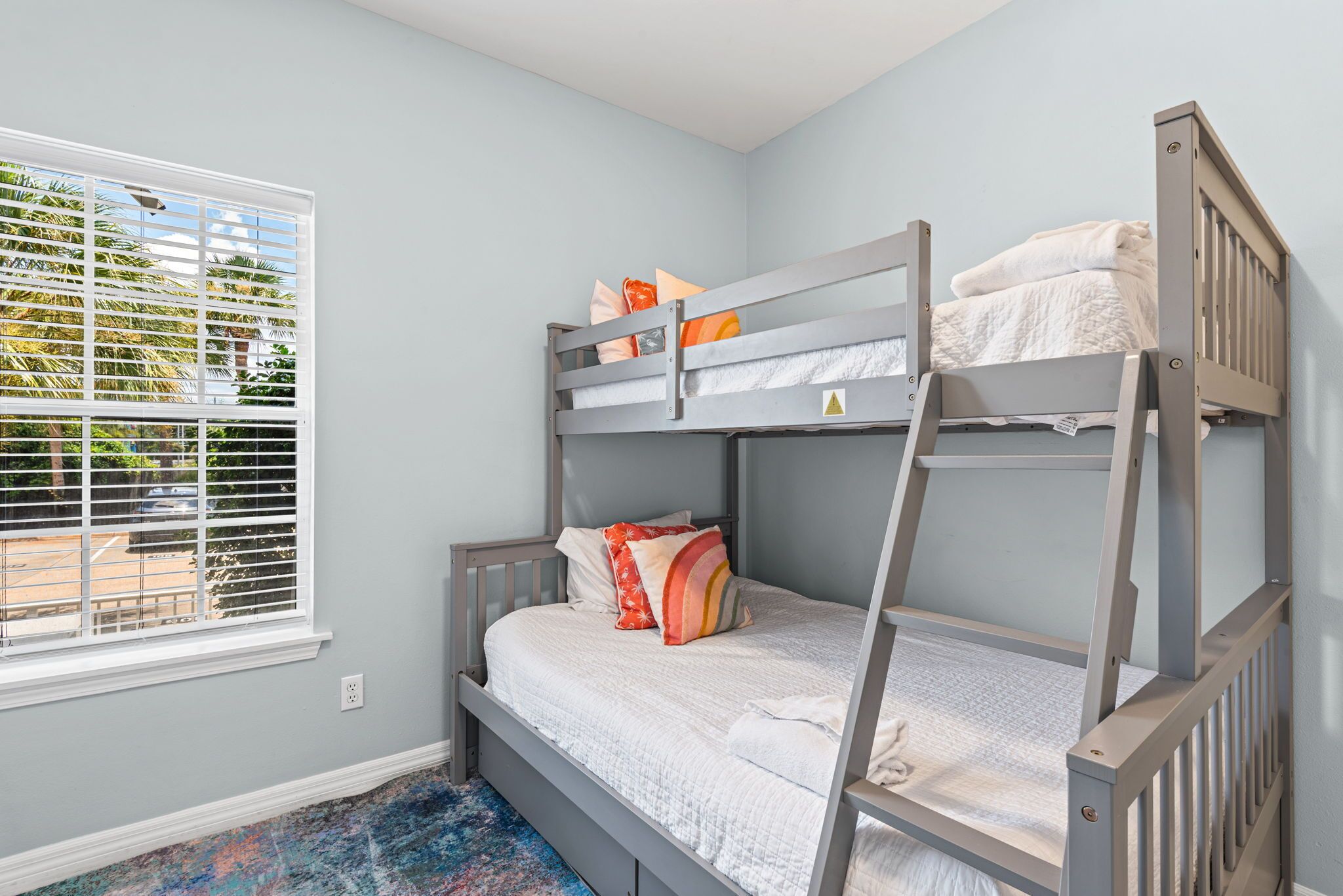 A bunk bed room with a window, a view of palm trees, and a blue carpet.