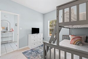 Une chambre d’enfant avec des lits superposés, une télévision, un bureau et une fenêtre avec des stores.