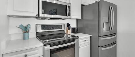 A modern kitchen with stainless steel appliances, including a microwave, oven, and refrigerator. There are white cabinets and a countertop with a toaster and a knife block.