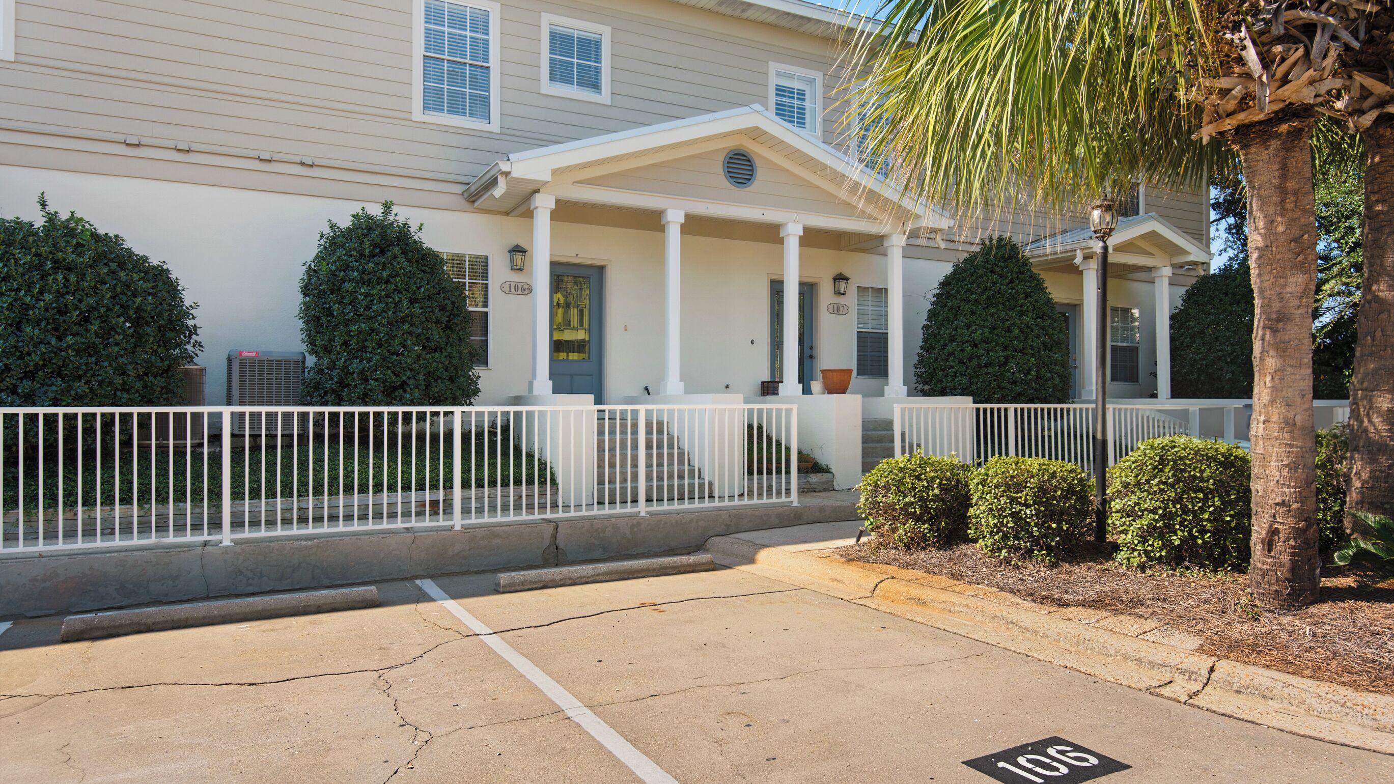 A two-story building with a covered porch, a parking lot, and a white fence.