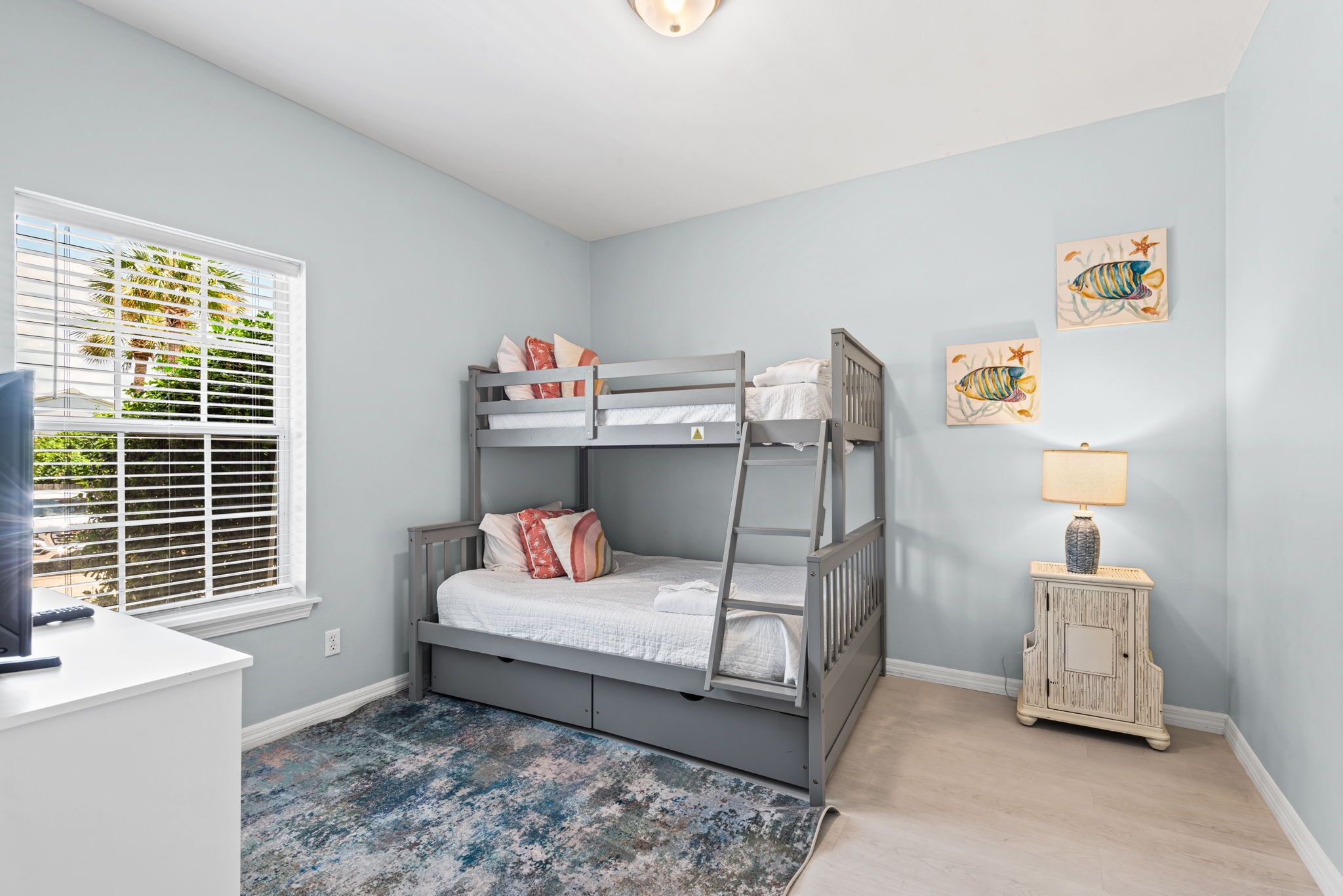 A bunk bed in a room with a window, a desk, and a small cabinet.