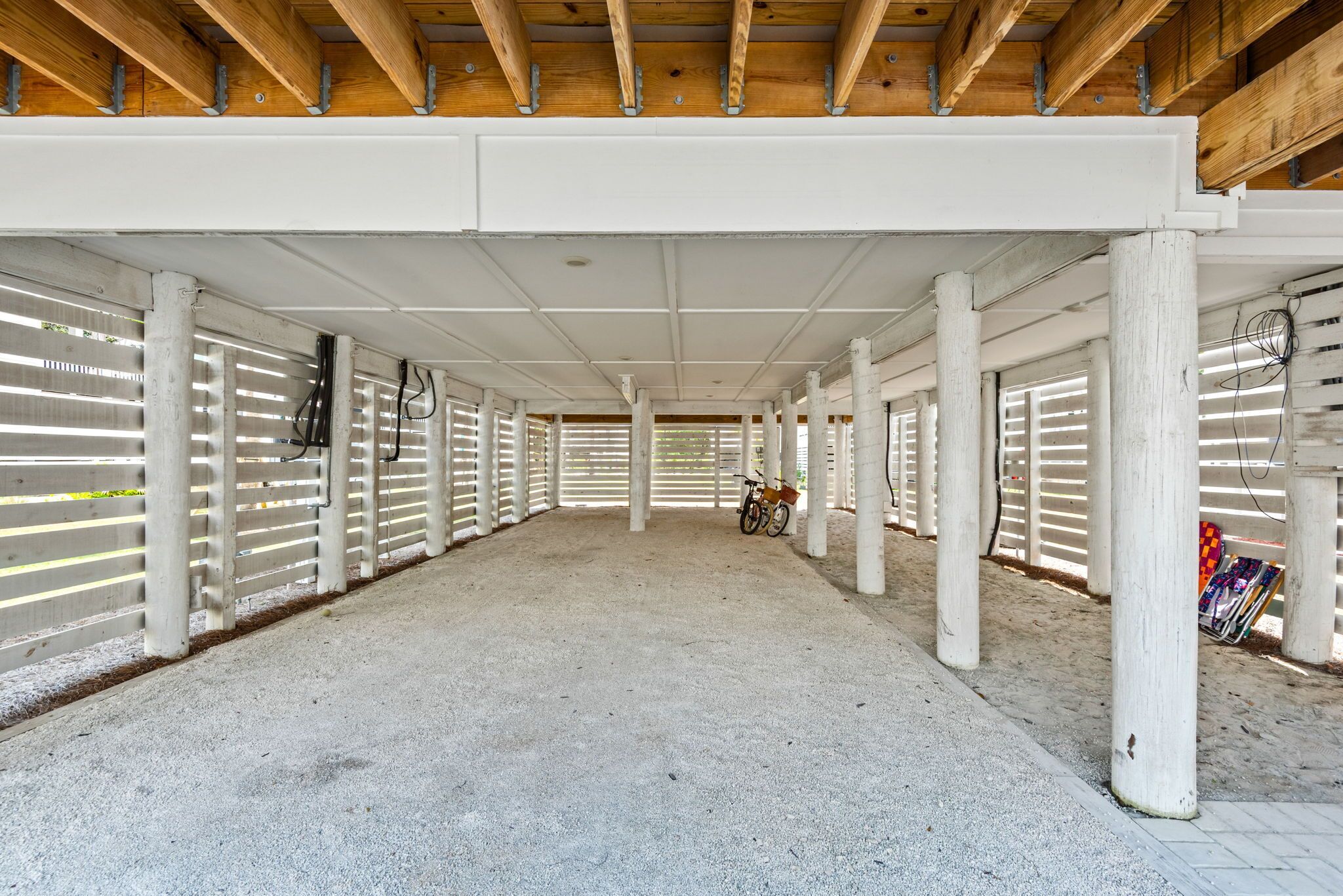 Una arena ecuestre techada en interior con suelo de hormigón, barandillas blancas y vigas de madera.