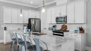 A modern kitchen with white cabinetry, a stainless steel refrigerator, a microwave, and a central island with bar stools. - 1-minute to the Boat Launch, Boat Parking Under Home, An Experience For Less (Santa Rosa Beach)