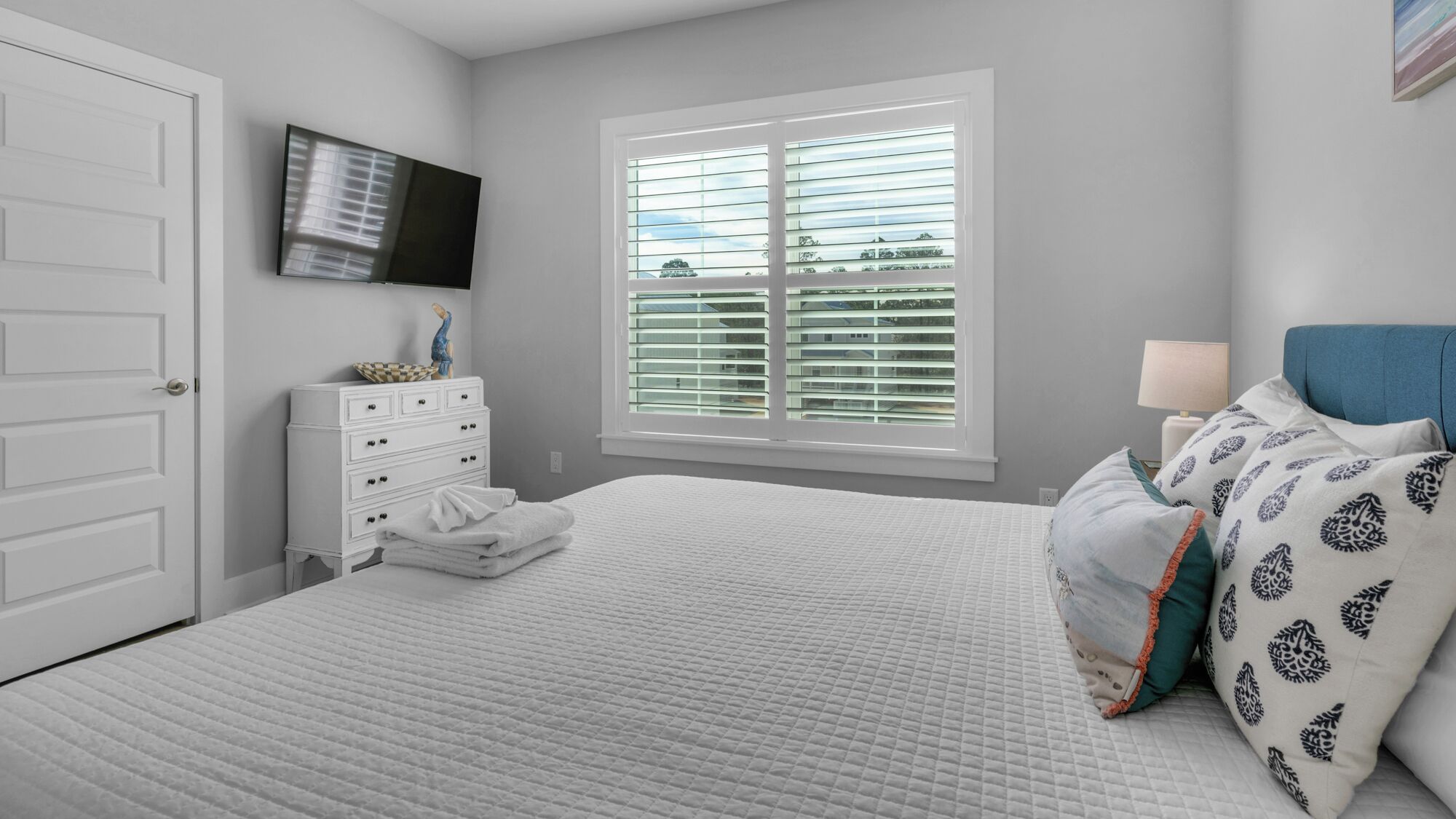 A bedroom with a bed, a dresser, a TV, and a window with blinds.