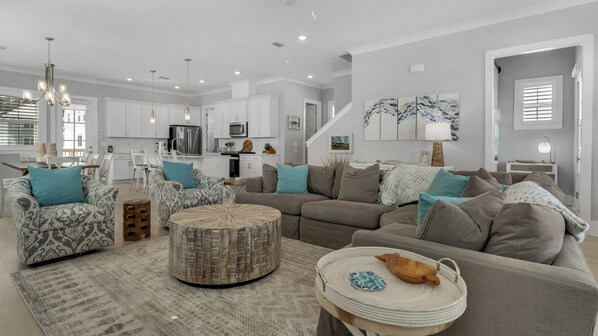 Relax in this stylish living space with a large L-shaped sofa, woven ottoman, and dining area.