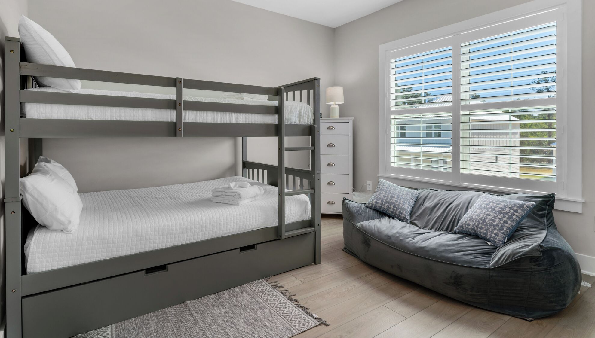 Quarto com beliche, sofá, abajur e janela com persianas.
