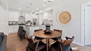 A modern kitchen with white cabinets, a central island, and a dining area with a round table and chairs. - Chic Bozeman Getaway - Minutes from Downtown! (Bozeman)