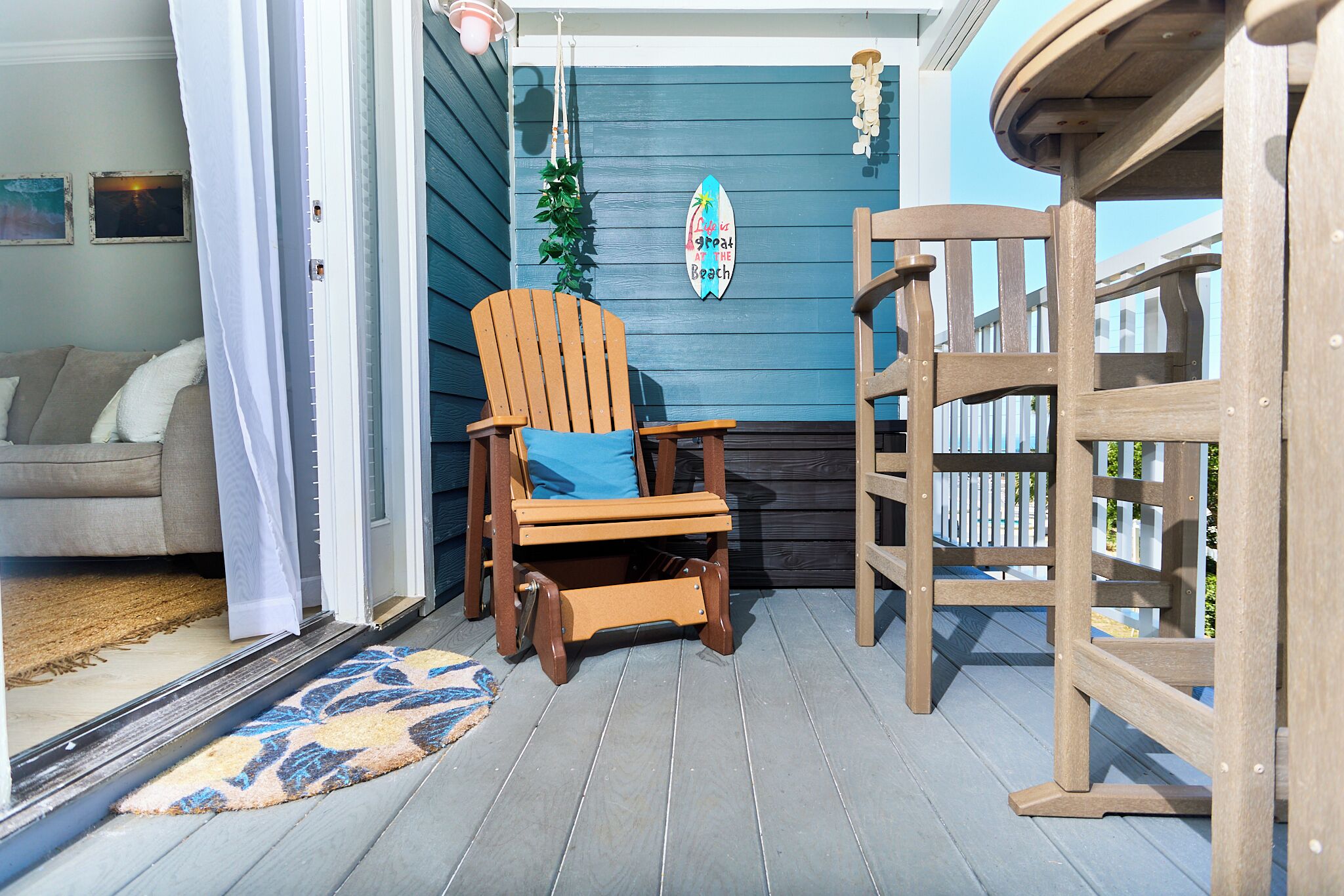Een houten terras met een stoel, een tafel, een deur en een muur met een decoratief bord.