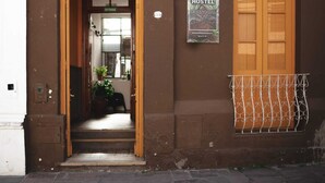 Entrada de un albergue con un letrero, una puerta de madera y una ventana con celosía de metal.