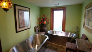 A bathroom with two large tubs, a chair, a vase with flowers, and framed artwork on the walls.
