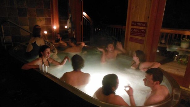 A hot tub with people sitting around it, a wooden deck, and a sign that reads 'NO DIVING CAPACITY'.