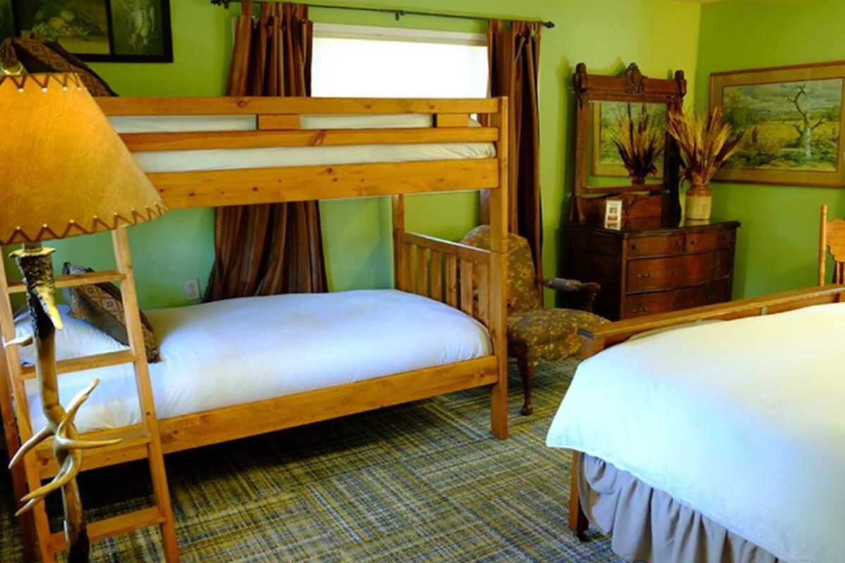 A room with a bunk bed, a wooden dresser, a lamp, and a painting on the wall.