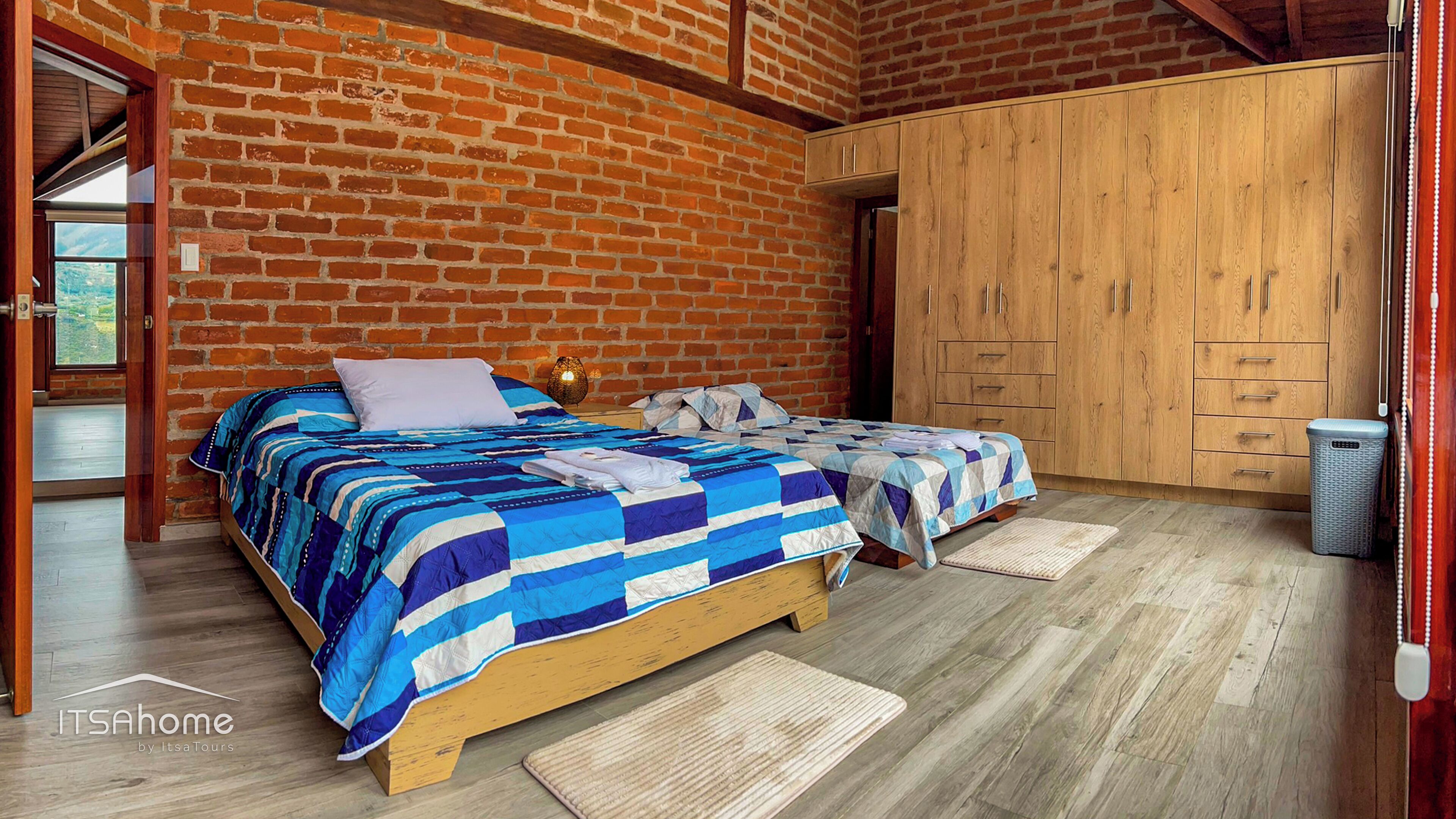 A bedroom with a wooden bed, a brick wall, and a wooden wardrobe.