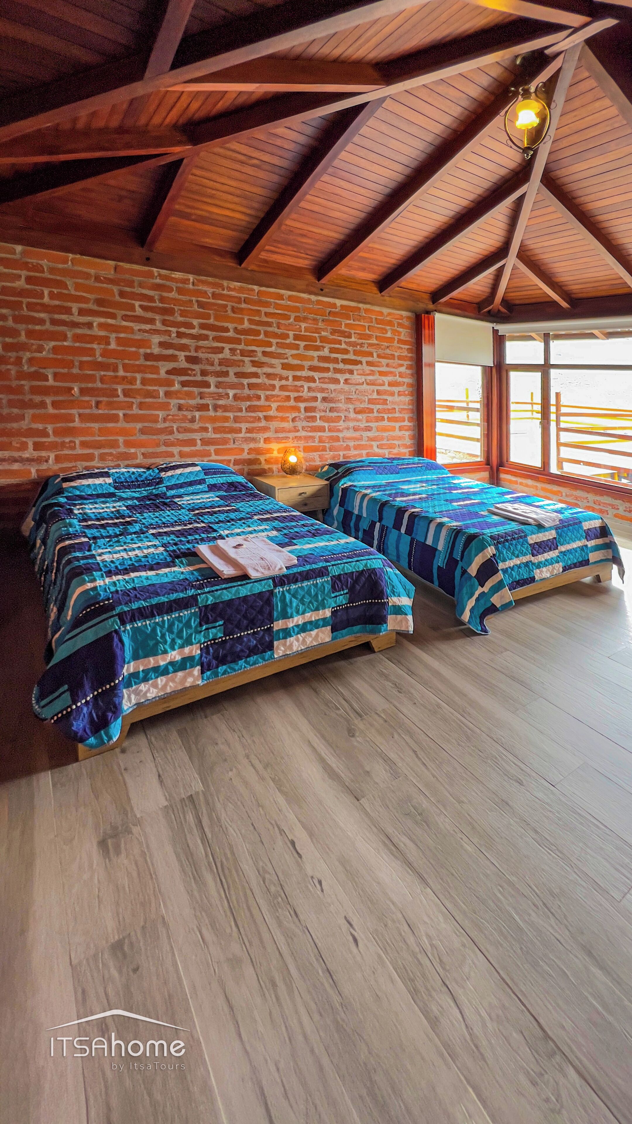 A room with two beds, a brick wall, wooden beams, and a large window.